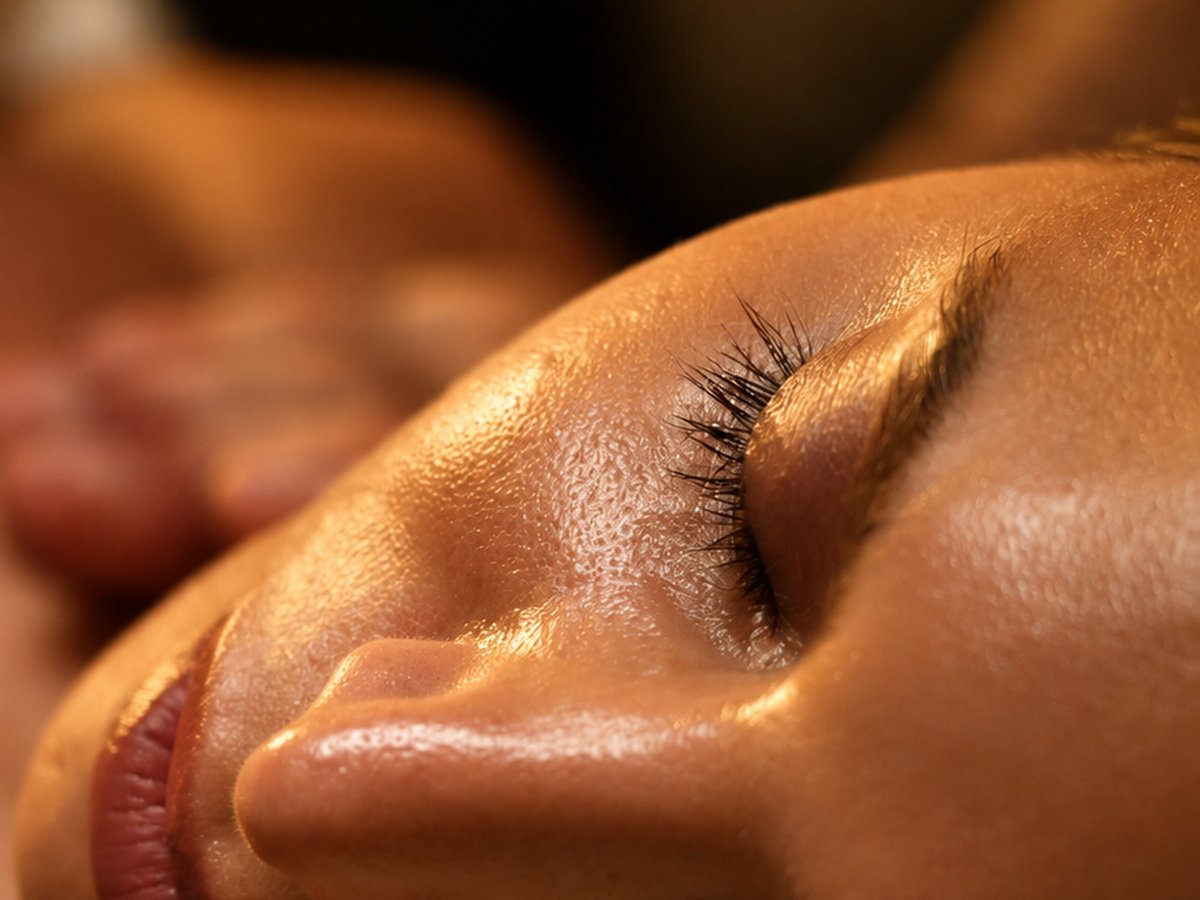 Primer plano del rostro de una persona con los ojos cerrados durante un masaje, con luz cálida