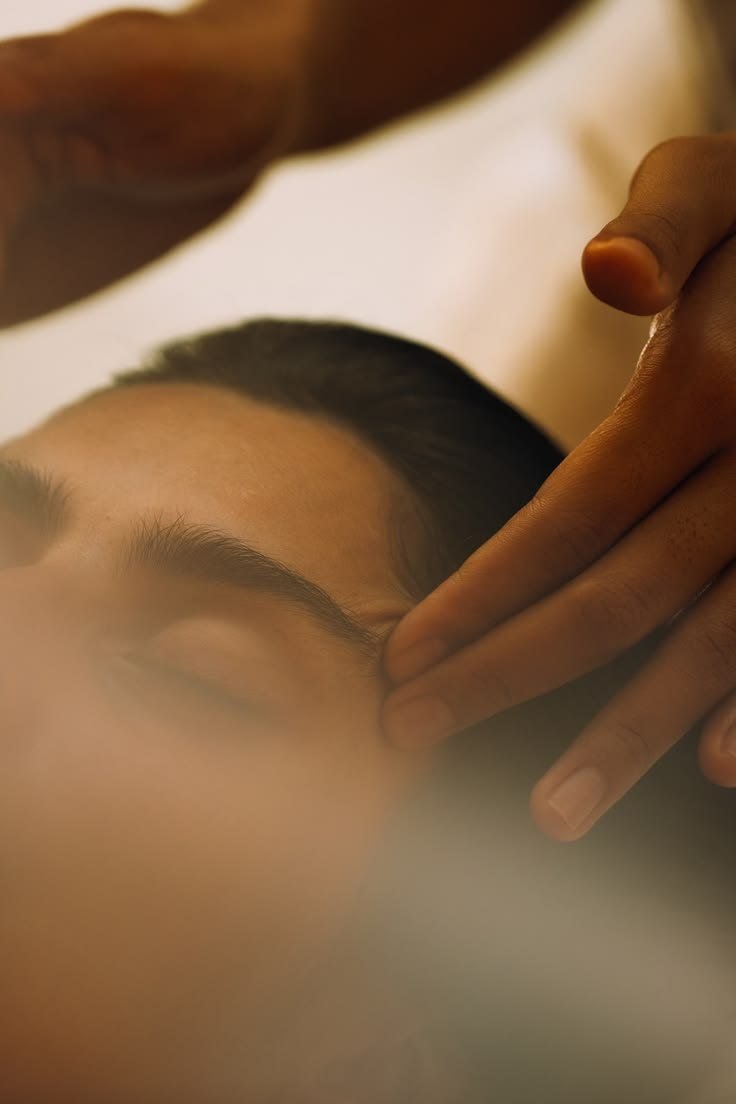 Rostro de una persona con los ojos cerrados mientras recibe un masaje, con las manos del terapeuta sobre su frente